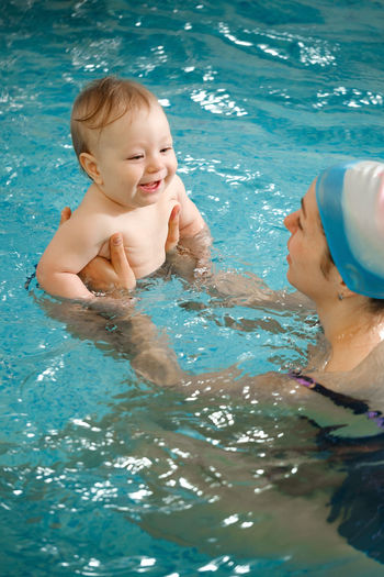 Early age swimming in pool. baby boy trained to swim in water. happy child with trainer woman in