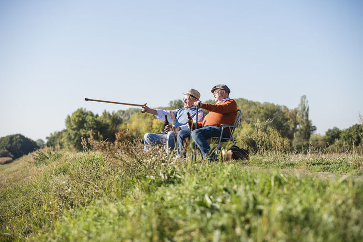 Two old friends sitting in the fields, drinking beer, pointing with walking stick
