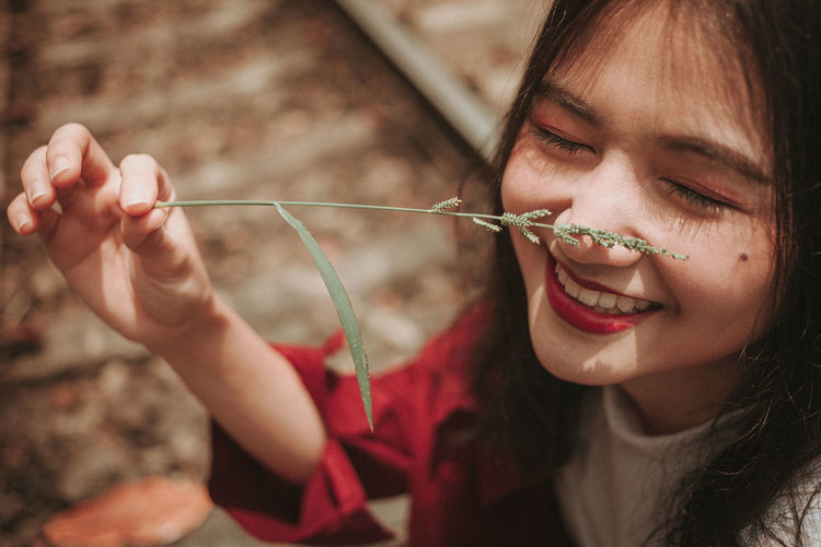 Close-up of smiling young woman holding plant on nose