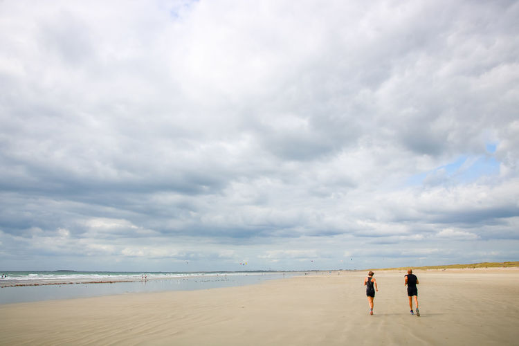 Rear view of people running on beach against sky