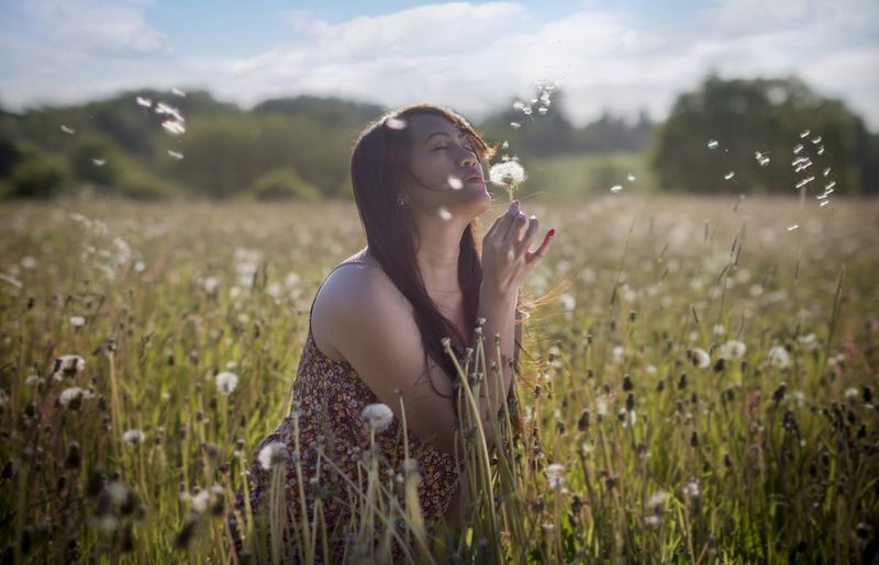 Teenage girl with eyes closed blowing dandelion on land