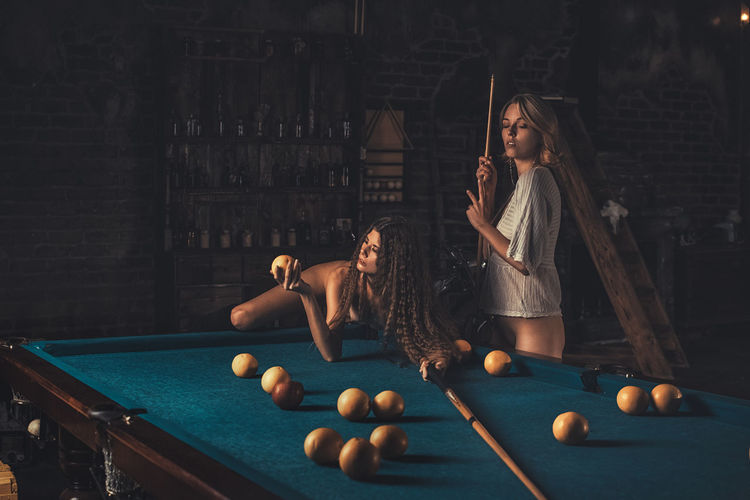 Two pretty young women are playing billiards. instead of balls on the table oranges