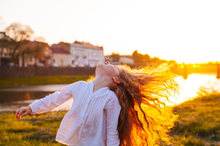 Woman with arms outstretched standing against sky during sunset