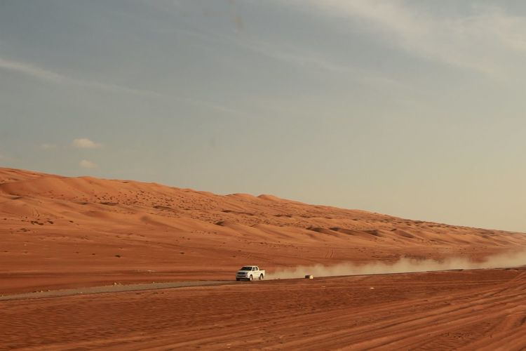 Car moving on street amidst field in desert against sky