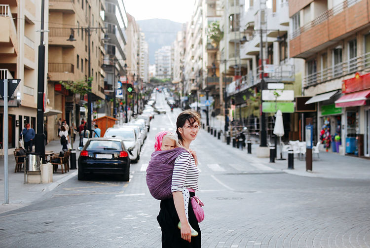Portrait of woman with baby on back walking on street in city