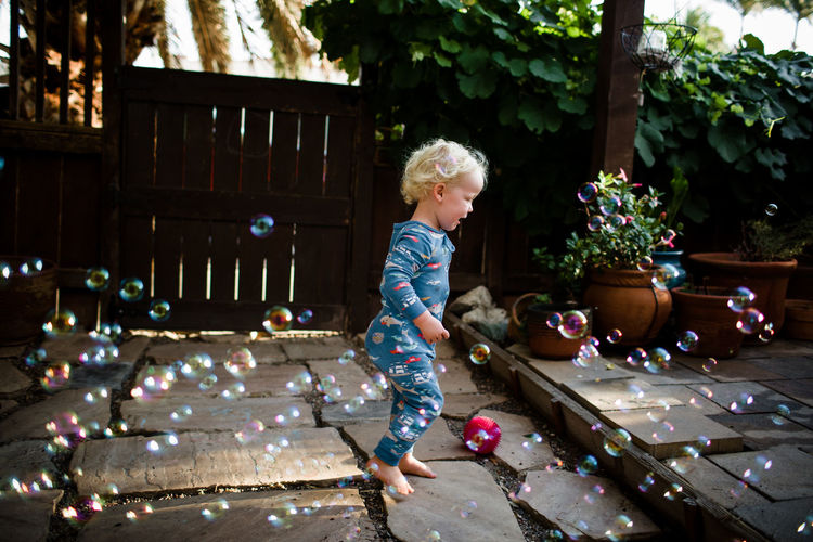 Two year old in pajamas running through bubbles in front yard