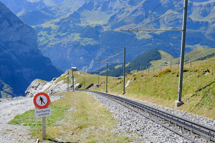 Road sign by railroad tracks against mountains