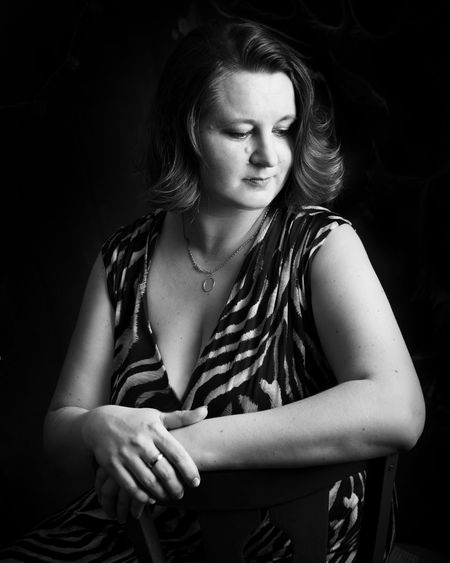 Thoughtful woman sitting on chair against black background