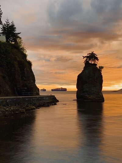 Rock formation on stanley park seawall path near sea against sky during sunset