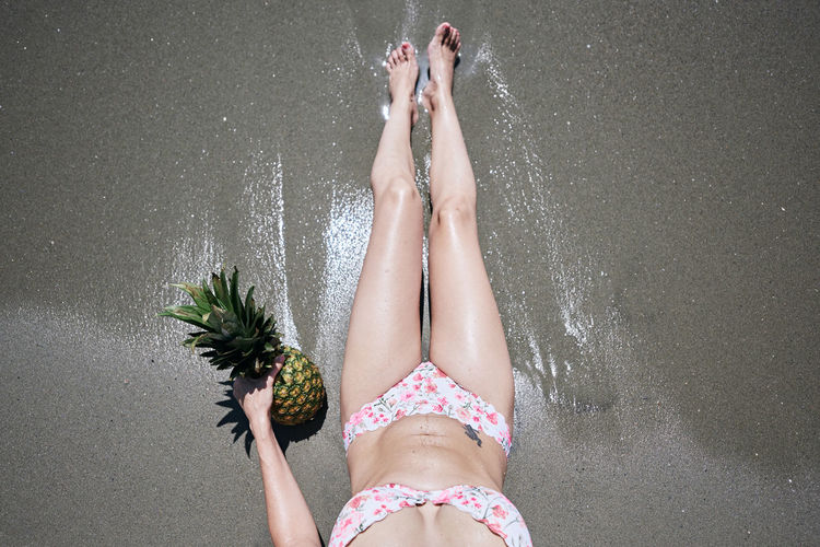 A young girl in a bikini lying on the sand on the beach with a pineapple. vacation concept