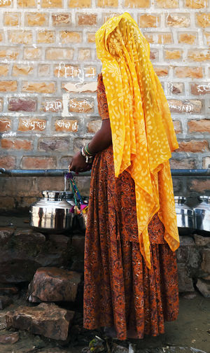 Rear view of woman in traditional clothing filling water in container