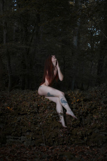 Naked hipster woman sitting in forest