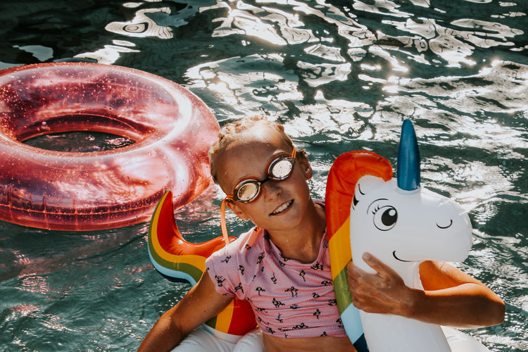 High angle portrait of smiling girl on unicorn inflatable in water