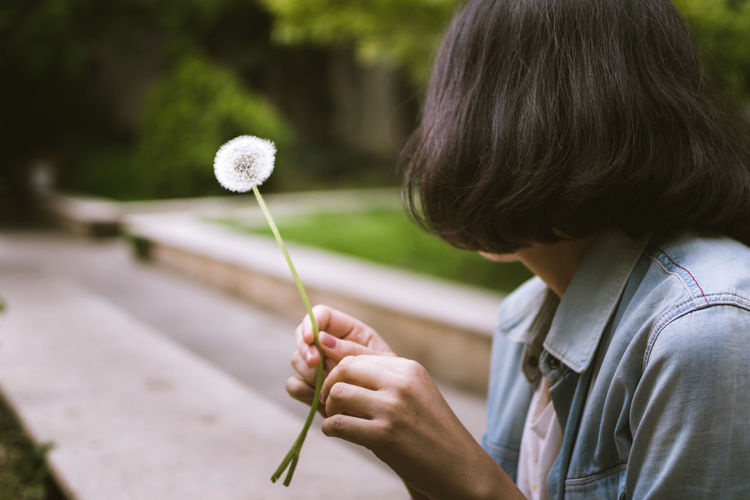 Close-up of woman holding dandelion while sitting in park