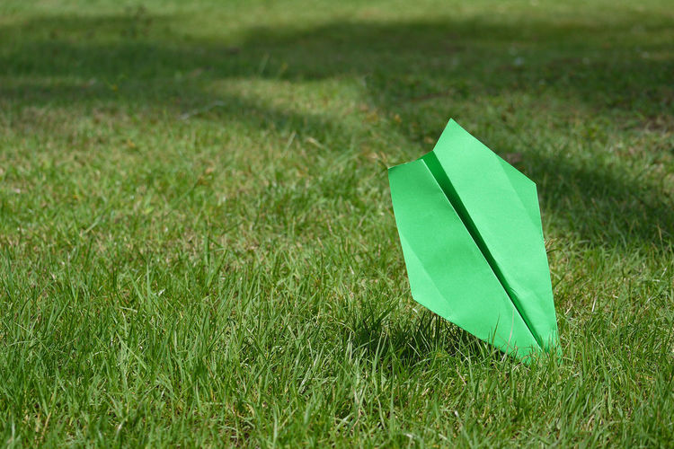 Green paper airplane on grassy field