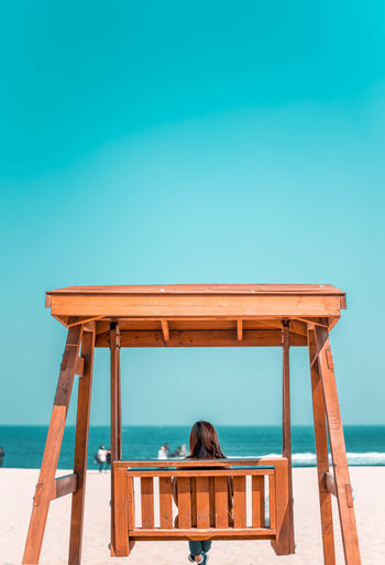 Woman sitting on swing at beach against clear sky