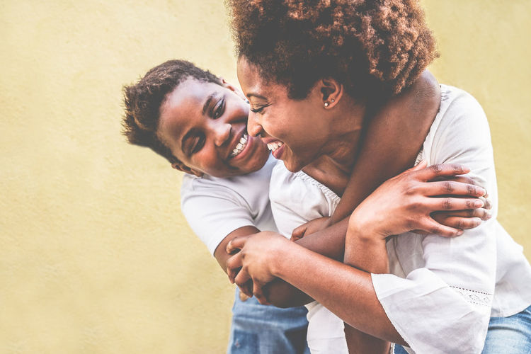 Happy son holding mother against yellow wall