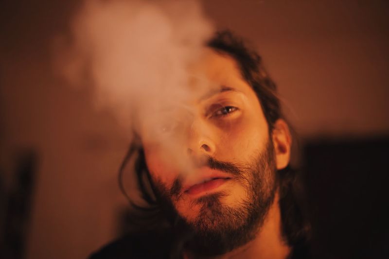 Portrait of young man exhaling smoke at home