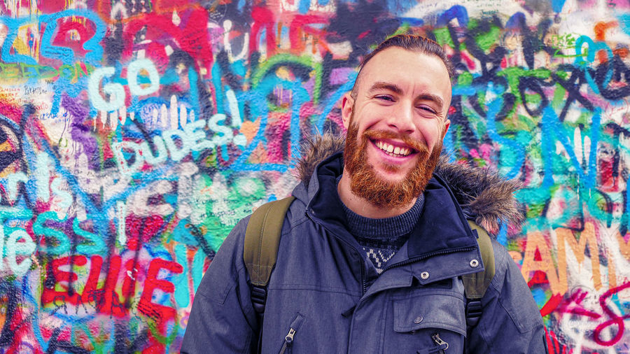 Portrait of a smiling young man against graffiti wall