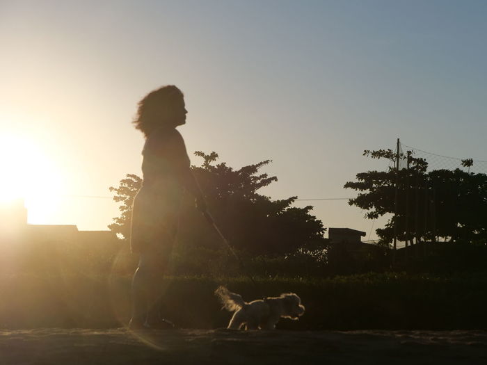 Side view of man with dog against sky during sunset