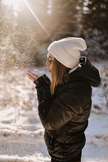 Side view of woman blowing snow while standing outdoors during winter