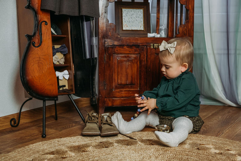 Cute little toddler baby girl in vintage clothes playing with beads at home. gender-neutral baby