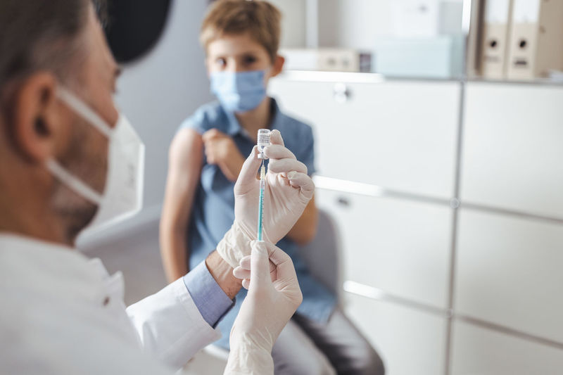 Healthcare worker preparing vaccine syringe for boy in background