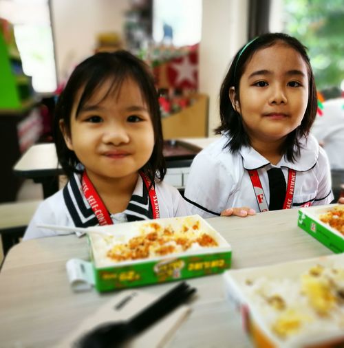 Portrait of sisters in school uniform having food on table at cafe