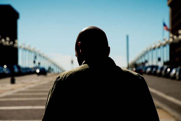 Rear view of man standing on bridge against sky in city