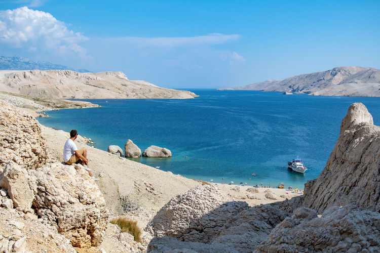 Young man sitting on cliff overlooking spectacular beach on pag island in croatia.