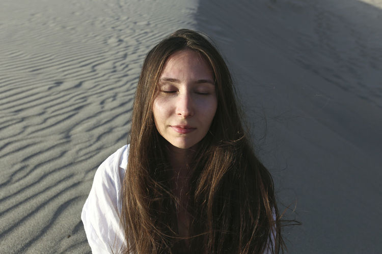 Young woman with eyes closed sitting on beach