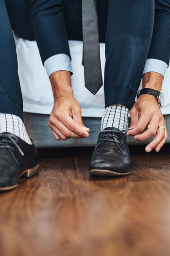 Low section of man tying shoelace on hardwood floor