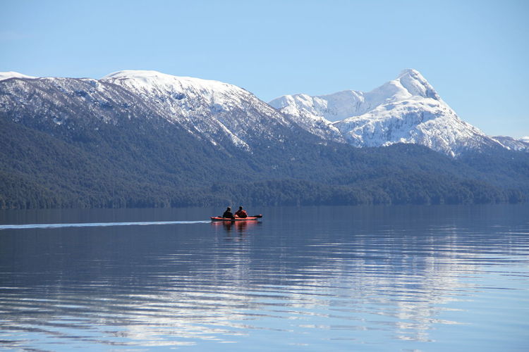 People kayaking on lake against mountains