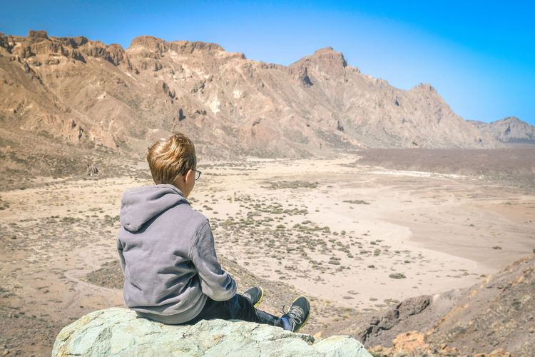 Boy sitting on rock at desert