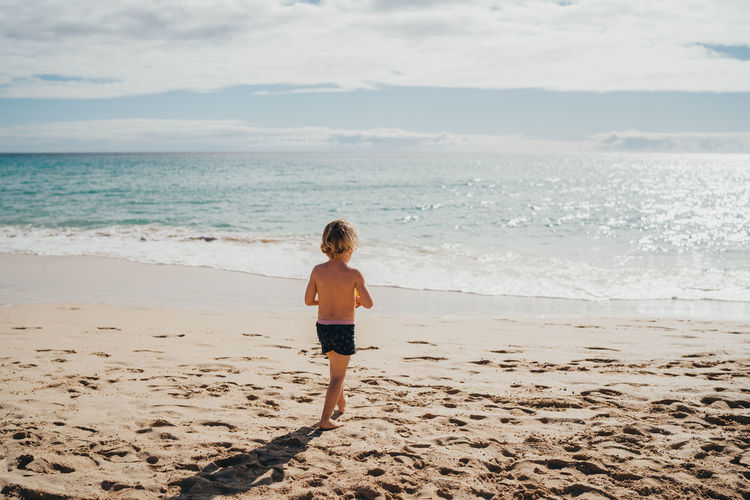 Boy walking into the water at the beach on a sunny day on vacation