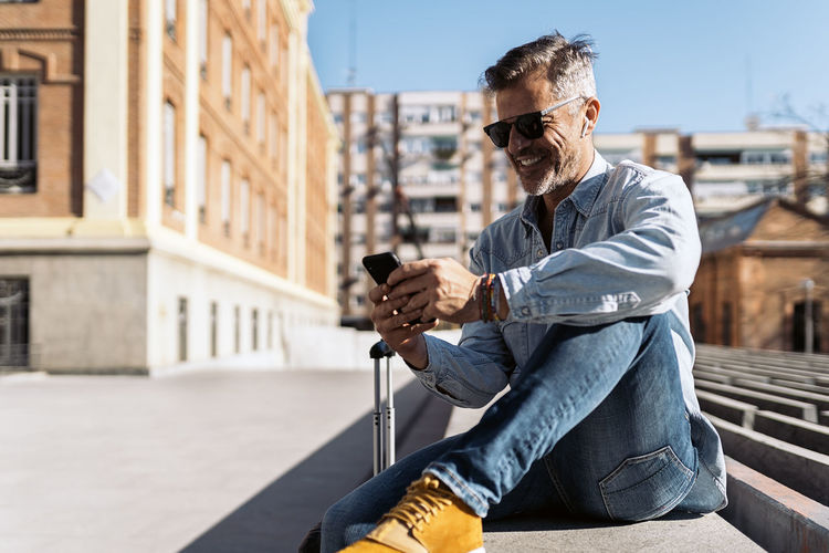 Man wearing sunglasses sitting on sidewalk in city