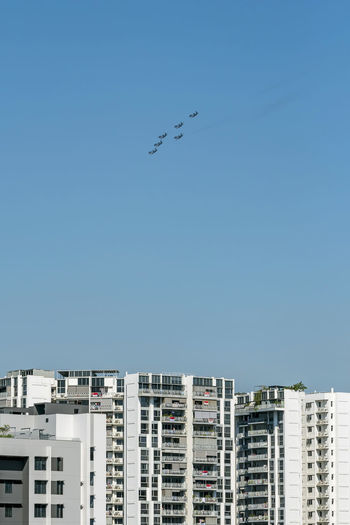 Low angle view of buildings against clear blue sky with airplanes flying overhead