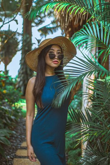 Young woman wearing hat standing against palm trees