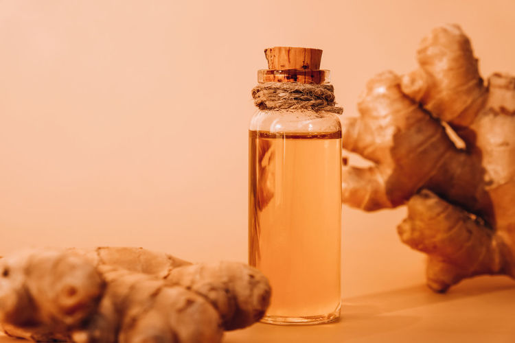 Glass bottle of essential ginger oil, ginger root on beige background. healthy food eating concept.