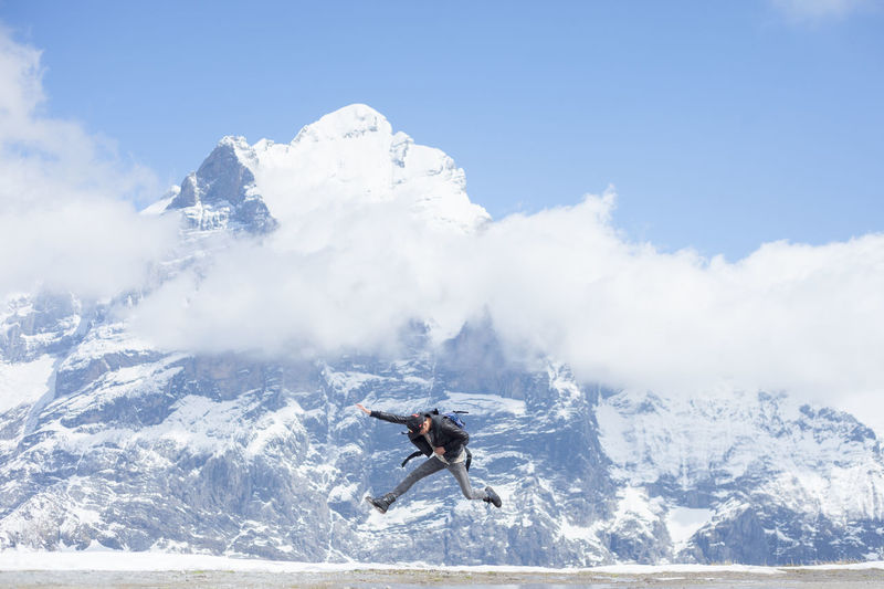 Excited man jumping against snow covered mountain