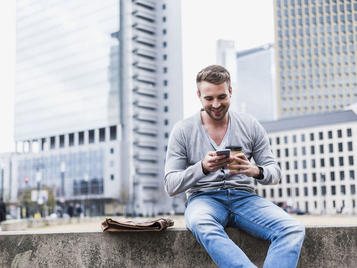 Young man using mobile phone while sitting in city