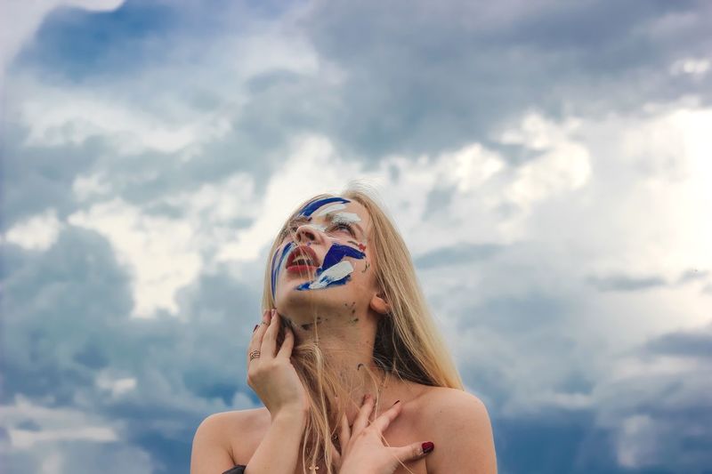 Young woman with face paint against cloudy sky