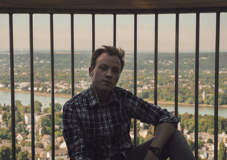 Portrait of young man sitting against railing