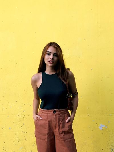 Portrait of beautiful young woman standing against yellow wall