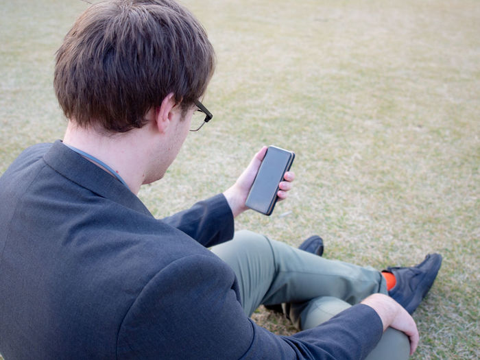 Rear view of man using mobile phone while sitting on grass