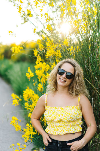 Young woman wearing sunglasses standing by yellow flower