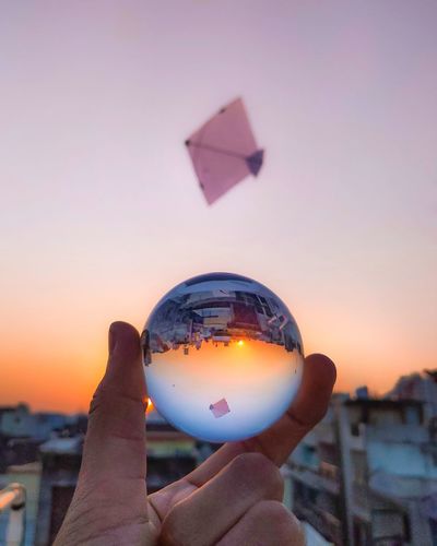Close-up of hand holding crystal ball against sky during sunset