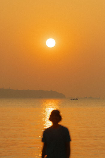 Rear view of man standing in sea against sky during sunset