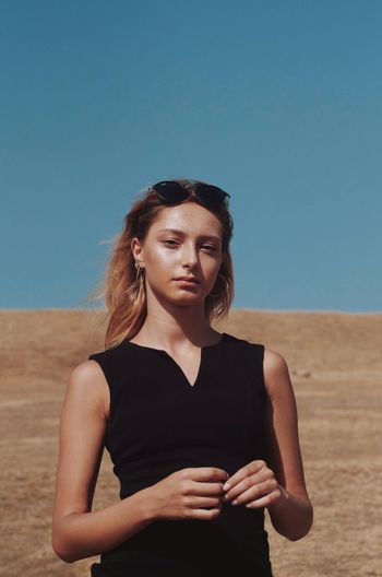 Portrait of beautiful young woman standing in desert against clear blue sky