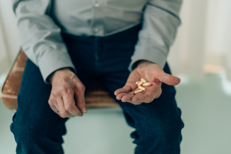 Midsection of senior man sitting on chair holding medicine pills in palm - fucus on fingers